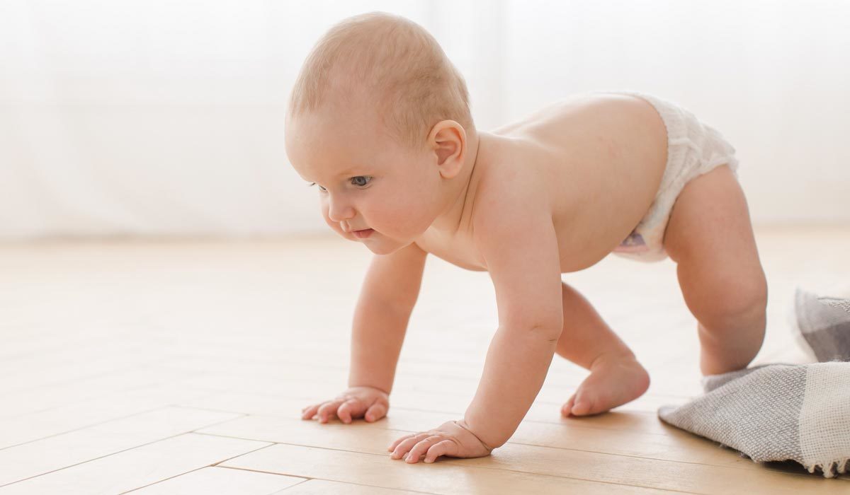Baby in einer Windel krabbelt auf einem Holzboden vor einem weichen, natürlich hellen Hintergrund und erkundet die Welt mit Holzspielzeug.