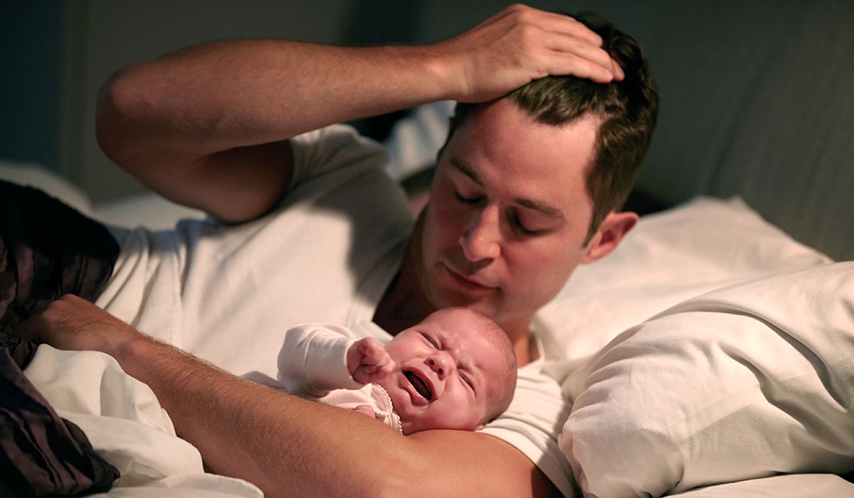 Mann mit schreiendem Baby im Arm im Bett
