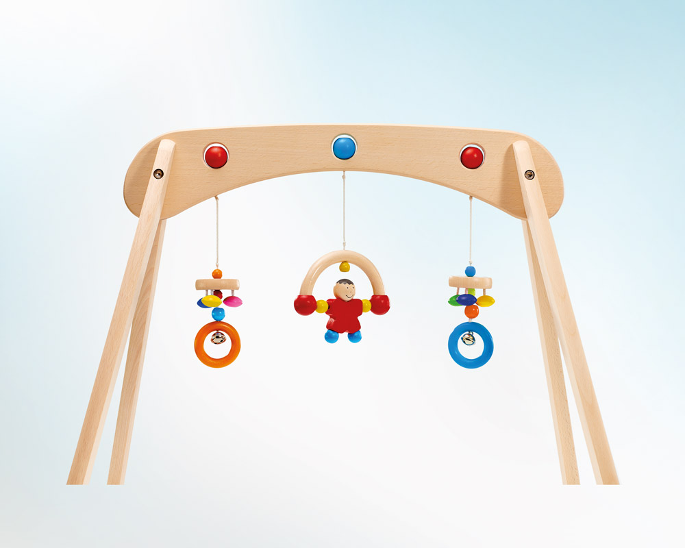 Musina Babygymnastik aus Holz mit bunten Spielsachen, wie Ringen und einer Figur, auf hellblauem Hintergrund.
