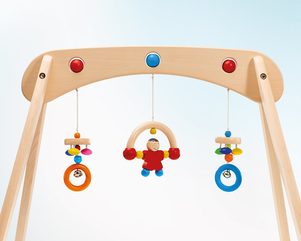 Musina Babygymnastik aus Holz mit bunten Ringen und einer lächelnden Figur auf hellblauem Hintergrund.