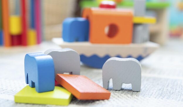 In dieser verspielten Krippenumgebung sind bunte Spielzeugelefanten und Bauklötze aus Holz auf einem Teppich verstreut.