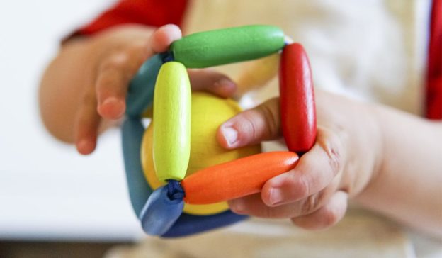 Babyhände erforschen ein dreidimensionales Holzspielzeug