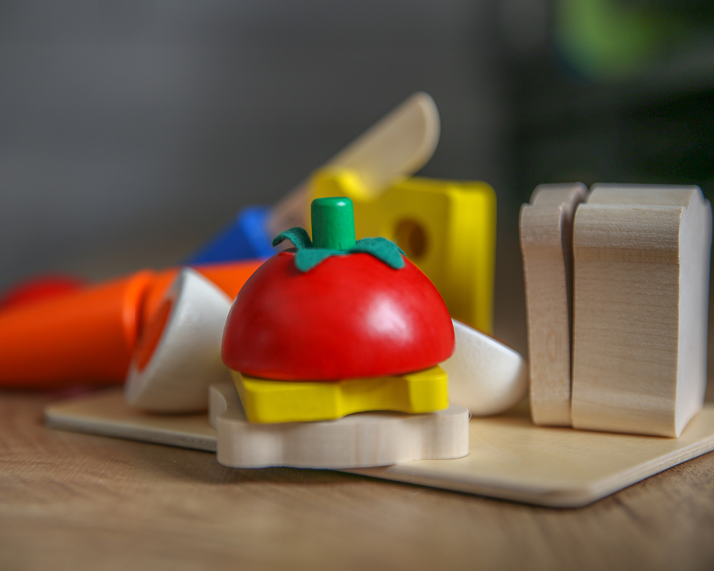 Holzspielzeug für Kind, einschließlich Gemüse essen wie Tomate, Käse und Brot auf einer Holzoberfläche.