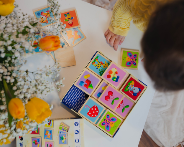 Ein Kind in einem gelben Pullover spielt mit Tierpuzzle-Blöcken und hilft der Sprachentwicklung an einem weißen Tisch mit Blumen.